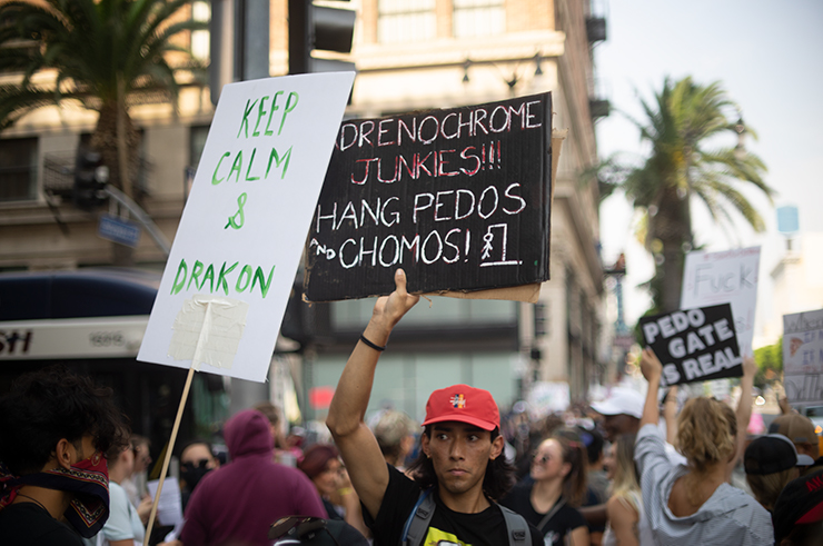 A man in a MAGA hat with a sign that says 'Adrenocrhrome Junkies!! Hang Pedos and Chomos! 'Chomo' is slang for child molester.