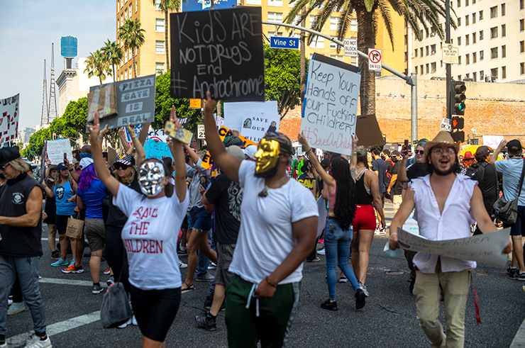 People holding up signs in the intersection of Hollywood and Vine. One sign says 'Kids are not drugs. End Adrenochrome.'