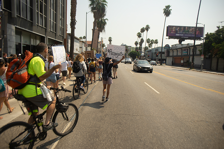 A woman holds a sign that says '#Pizzagate' while the QAnon rally marches to Hollywood High.