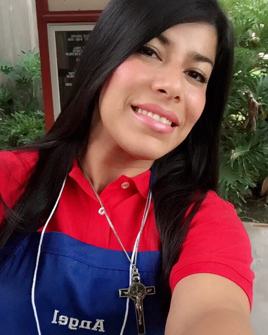 A smiling woman with a cross around her neck and an apron that says 'angel' on it.