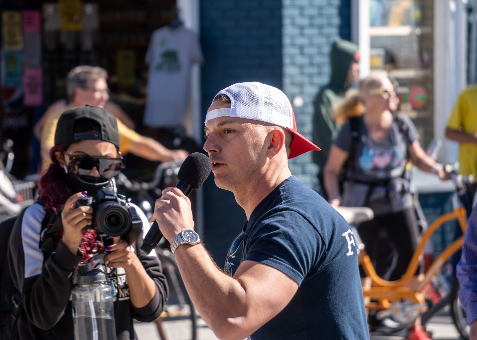 Chiropractic doctor and holistic medicine practitioner Cordie Williams speaks into a microphone while a photographer captures the moment. He is wearing a 1776 Forever Free shirt.