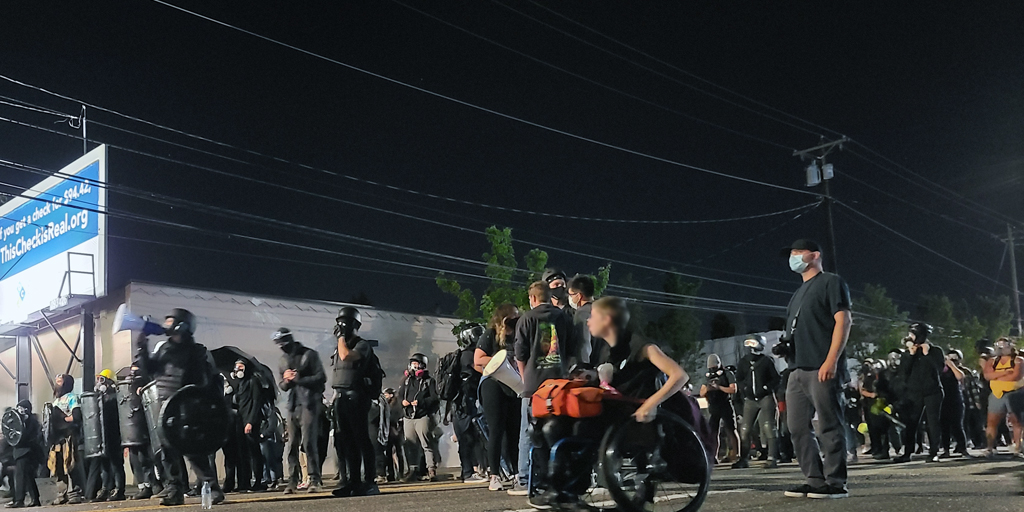 After about eighteen minutes, (and one dumpster fire in the middle of the east barricade line) riot officers begin forming up real lines for an advance down North Lombard. A shield phalanx rapidly forms in response for cover. Photo by James O'Ryan.