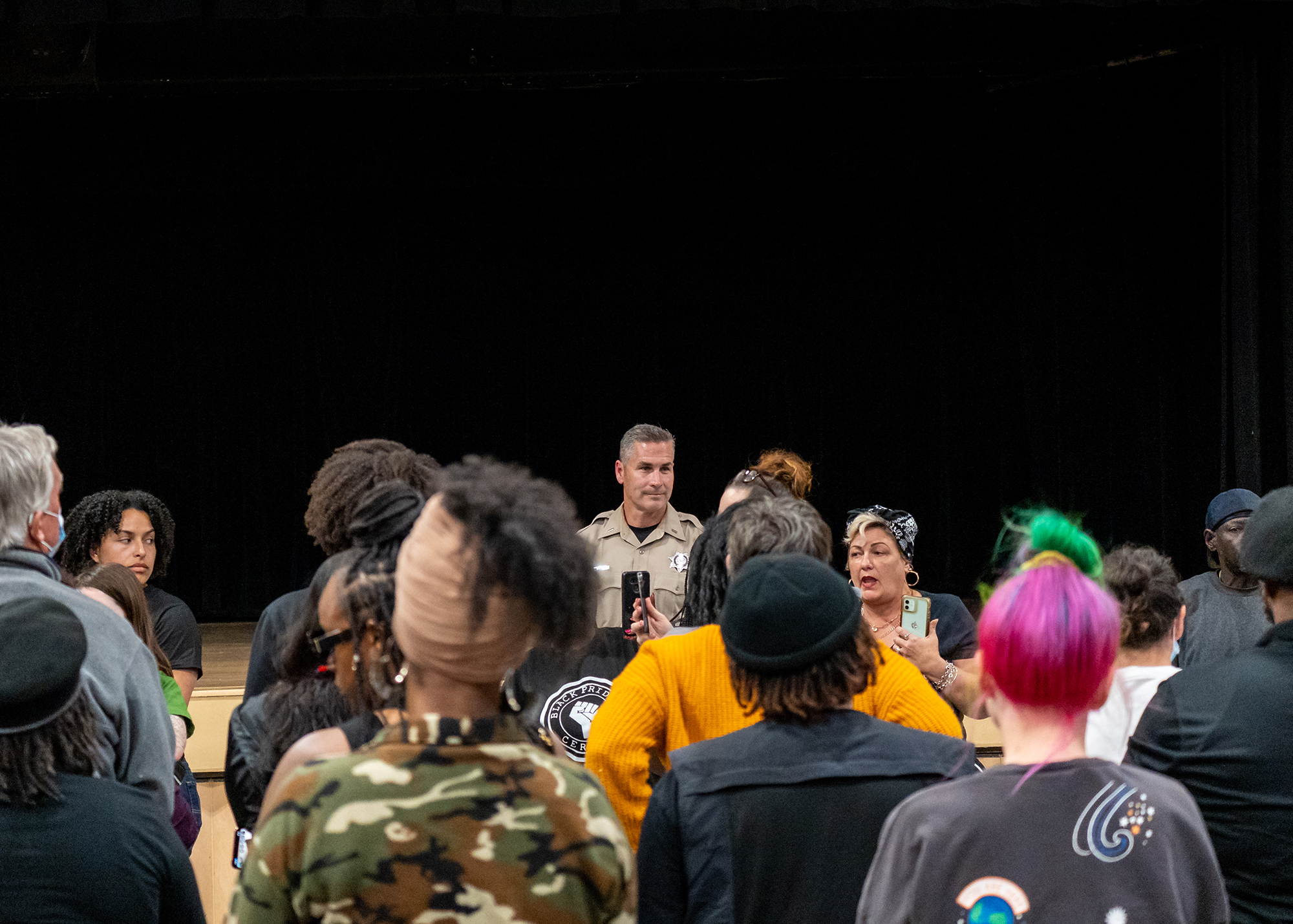 A crowd of people stand, visible from the upper shoulders and above, while Lt. Wray is in the middle of the frame, in focus and partially obscured by the crowd.