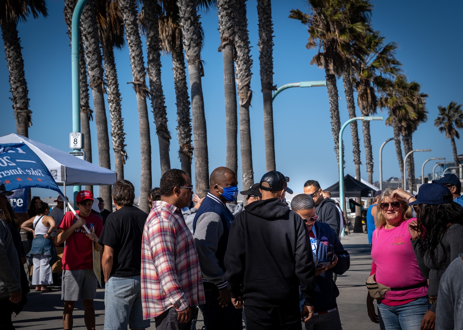 A small crowd of people talk while Joe Collins is again captured incidentally in the right third of the frame, looking down.