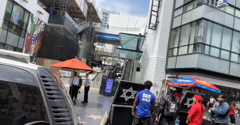 black men standing around a sign with a star of david on it, one wearing a blue shirt with white letters that say 'isrealite cult'