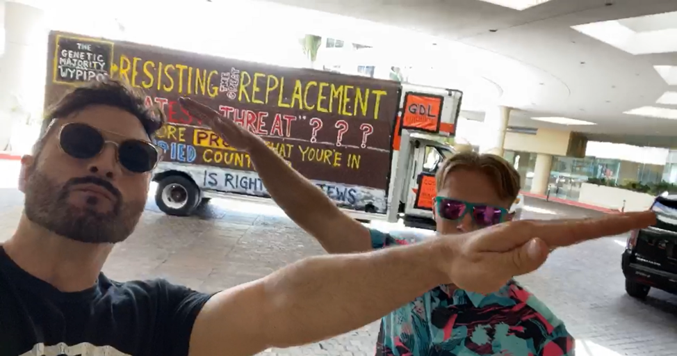 two men doing seig heils in front of their u haul truck, which is parked in the covered valet section of a hotel