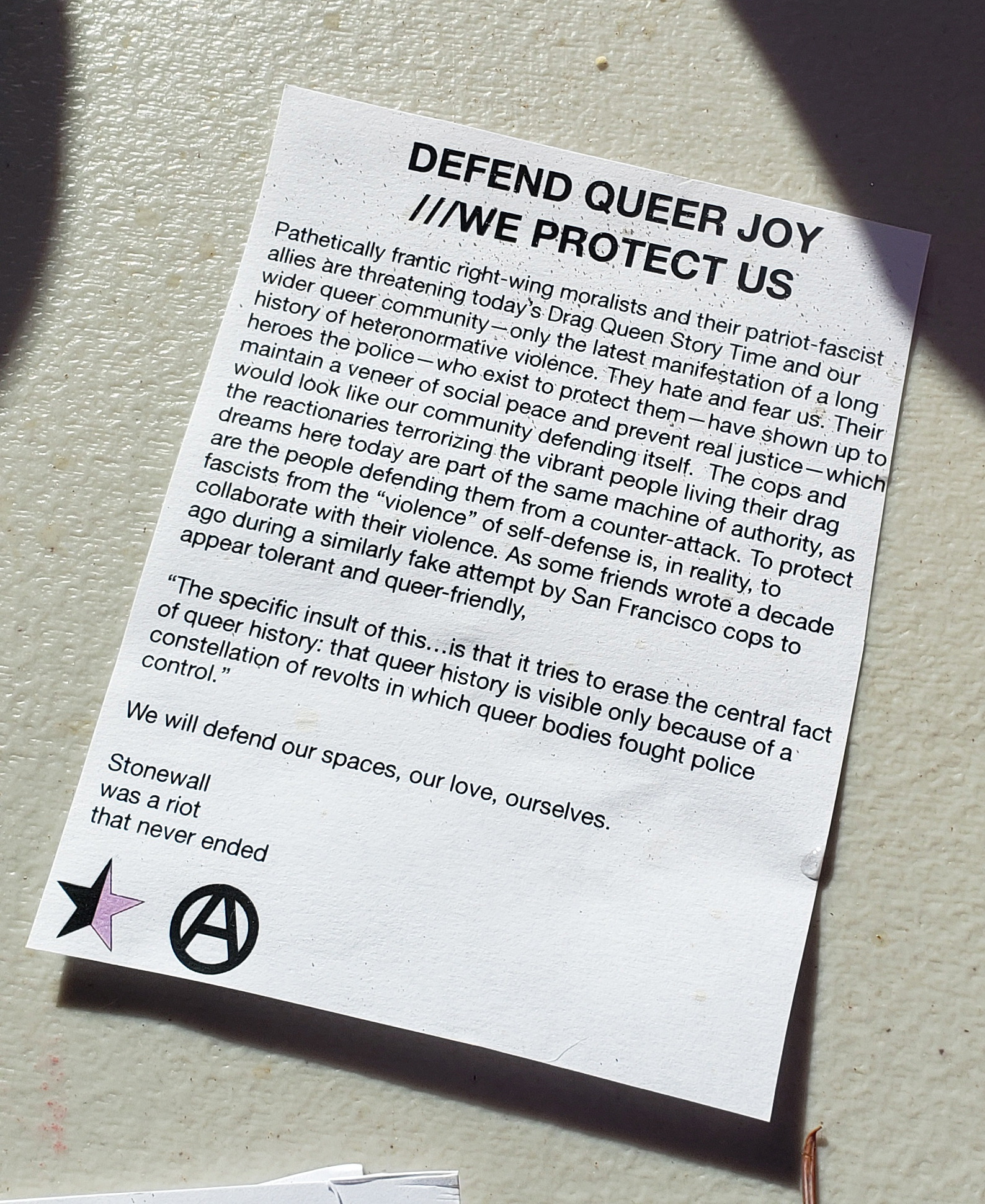 a paper handout on white paper with black text. It reads: 'DEFEND QUEER JOY  WE PROTECT US Pathetically frantic right-wing moralists and their patriot-fascist allies are threatening today's Drag Queen Story Time and our wider queer community only the latest manifestation of a long history of heteronormative violence. They hate and fear us. Their heroes the police who exist to protect them have shown up to maintain a veneer of social peace and prevent real justice which the reactionaries terrorizing the vibrant people living their drag dreams here today are part of the same machine of authority, as are the people defending them from a counter-attack. To protect fascists from the 'violence' of self-defense is, in reality, to collaborate with their violence. As some friends wrote a decade ago during a similarly fake attempt by San Francisco cops to appear tolerant and queer-friendly. 'The specific insult of this is that it tries to erase the central fact of queer history: that queer history is visible only because of a constellation of revolts in which queer bodies fought police control. We will defend our spaces, our love, ourselves. Stonewall was a riot that never ended'