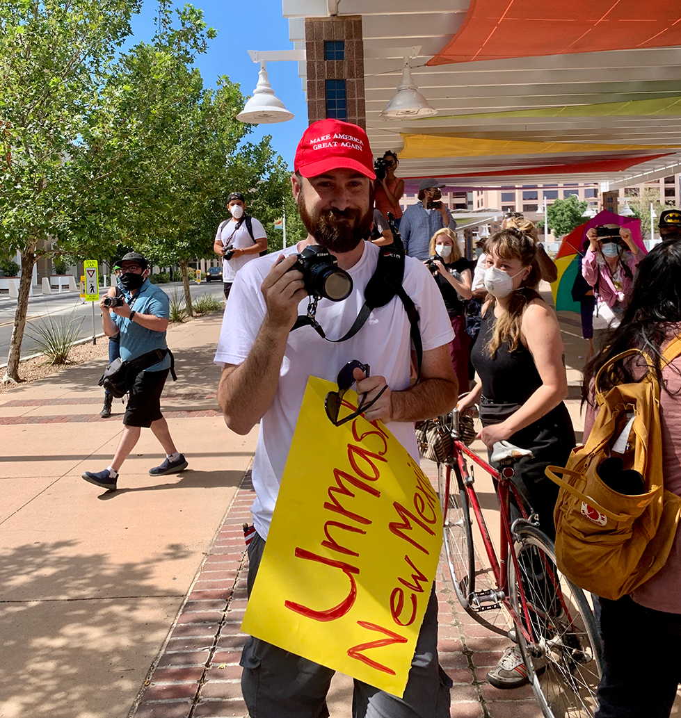 An anti-quarantine protester wearing a MAGA hat and holding a sign that reads 'Unmask New Mexico.' Photo by Bella Davis.