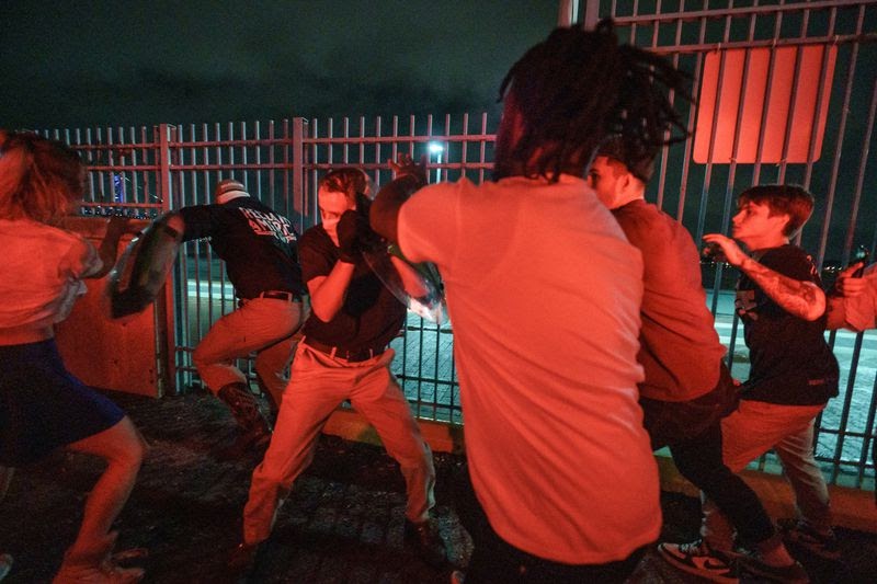 Bathed in red light in a parking lot near midnight, three Philadelphia residents push back Patriot Front members carrying plastic shields and wearing khaki pants.