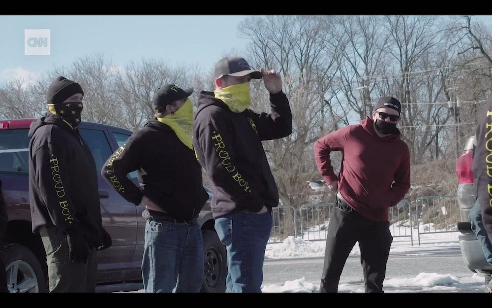 A screenshot from CNN video shows four men in yellow face coverings wearing black-and-yellow sweatshirts with 'PROUD BOY' written down the right arm. Another man in red wears a 'PROUD BOYS' cap.