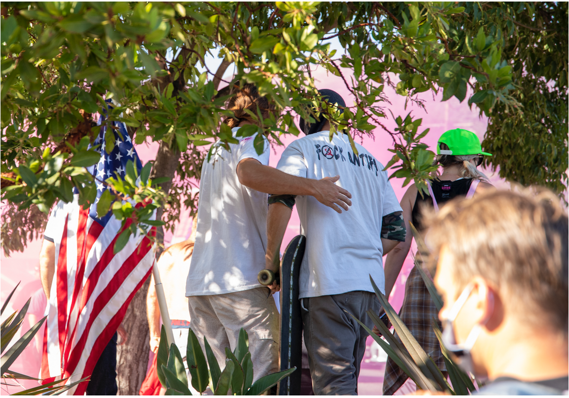 IMan in the “Fuck Antifa” shirt before using his board as a weapon. Pink smoke in the background.