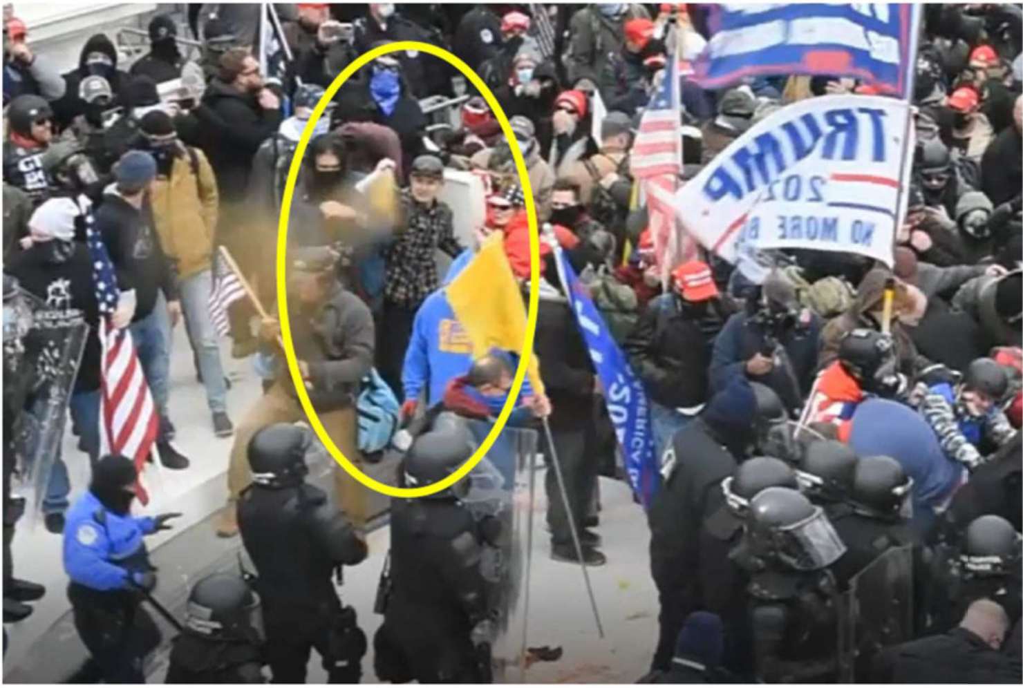 McHugh spraying a substance that looks like pepper spray at a line of cops in a grainy still from a video of the capitol riot.'