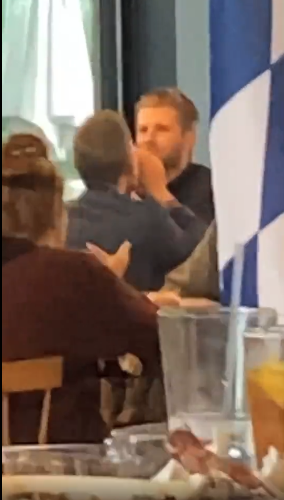 A blurry frame of a video showing a fair-skinned man in a suit eating at a table