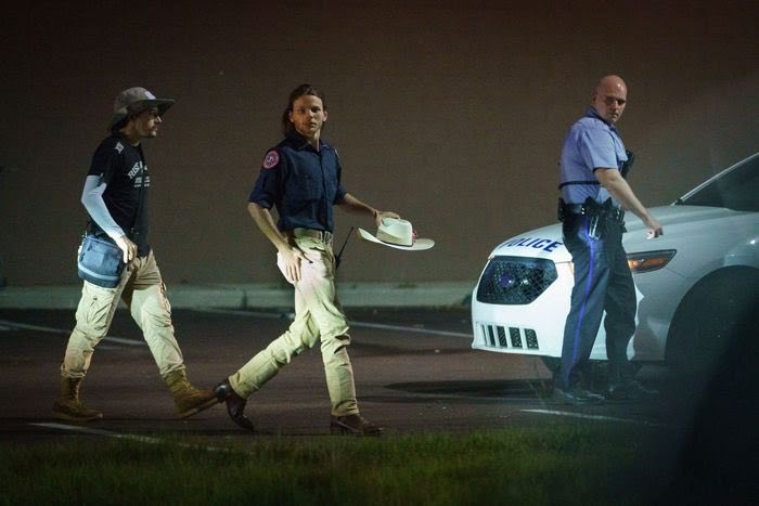 Photo of three men in Philadelphia, PA. From left to right: Graham Jones Whitson wearing khakis, boots, black shirt, bucket hat - Thomas Rousseau, wearing khakis, boots, Patriot Front shirt, cowboy hat - Police officer wearing blue shirt, black pants.