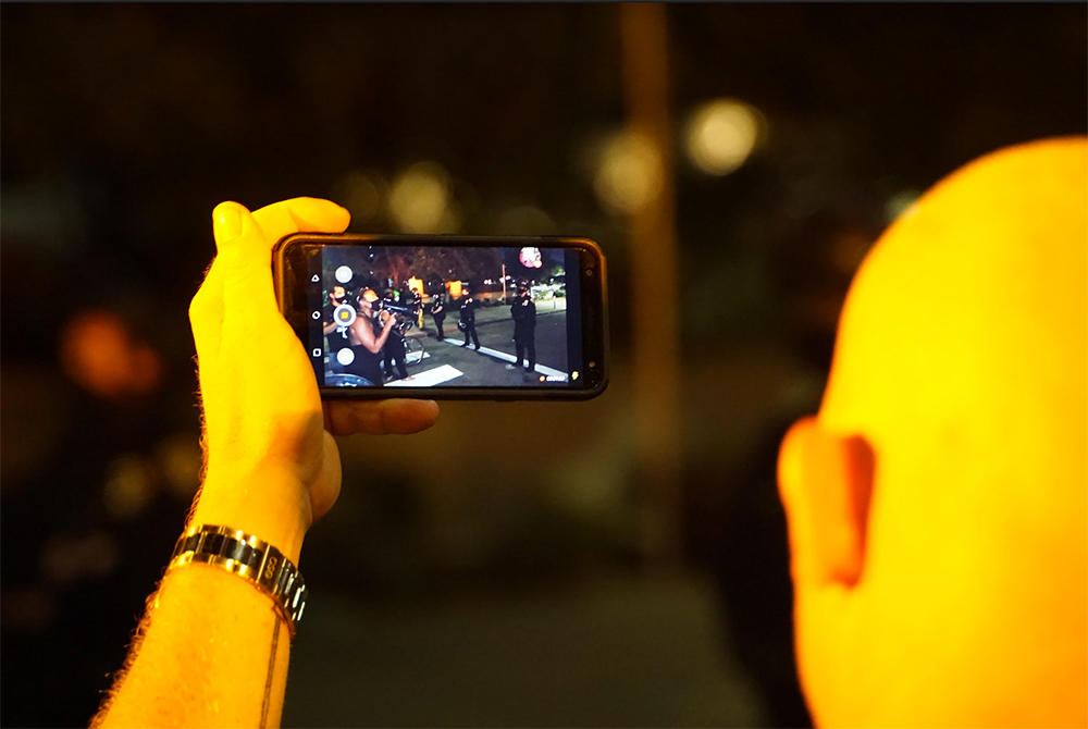 A protester records as others confront police. Photo by Tom Mann.